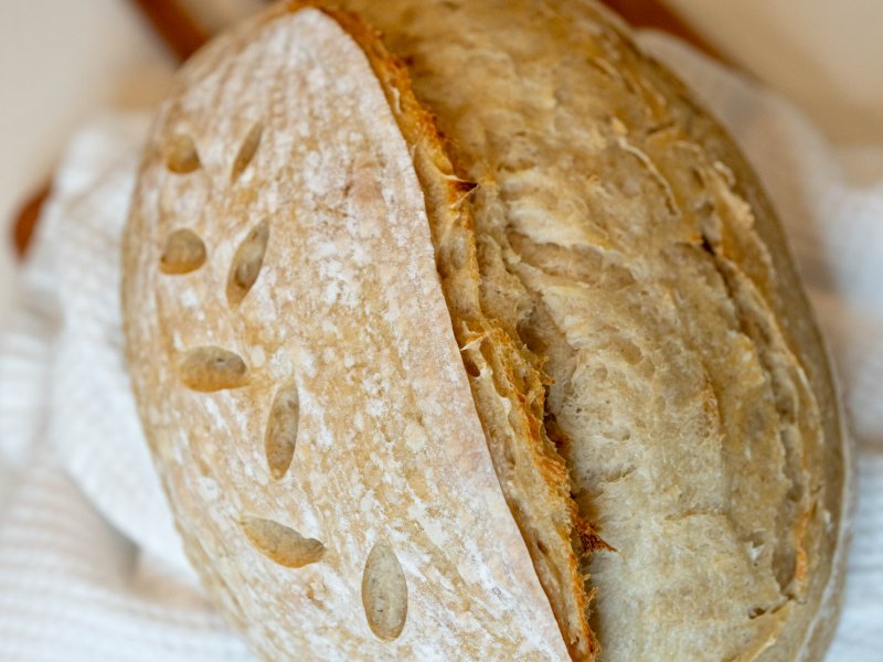 Golden oval sourdough loaf with a long curved score and leaf-shaped cuts, resting on a white towel and wooden board.